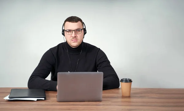 Hombre concentrado en auriculares usando portátil mientras está sentado sobre fondo gris con fondo — Foto de Stock