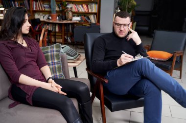 Genç hasta, özel ofisinde notlar alan terapistiyle konuşuyor.