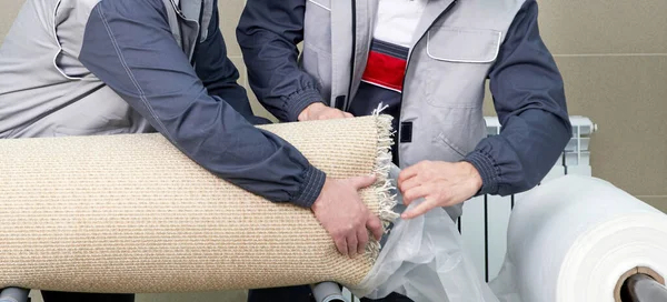 Los hombres trabajadores que embalan la alfombra en una bolsa de plástico después de limpiarla en lavadora automática y secadora en el servicio de lavandería —  Fotos de Stock