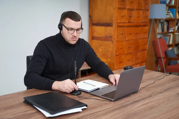 Hombre concentrado en auriculares usando portátil mientras está sentado sobre fondo gris — Foto de Stock