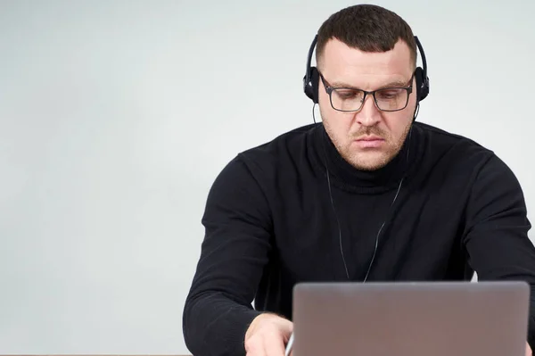 Hombre concentrado en auriculares usando portátil mientras está sentado sobre fondo gris con fondo — Foto de Stock