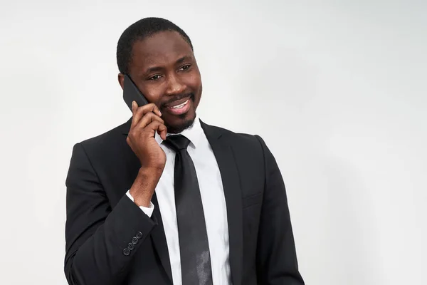 Retrato do homem africano sorrindo enquanto fala no telefone com parede cinza no fundo com espaço de cópia — Fotografia de Stock