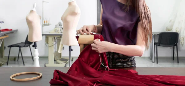 Beautiful young dressmaker in workroom sewing red dress in tailor studio or atelier shop — 스톡 사진