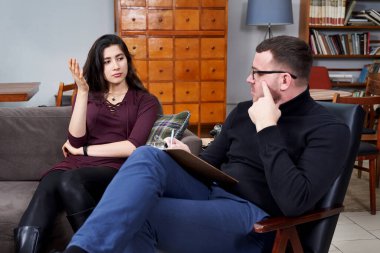 Genç hasta, özel ofisinde notlar alan terapistiyle konuşuyor.