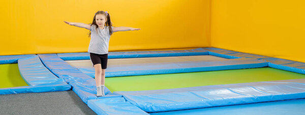 Счастливая улыбающаяся маленькая девочка прыгает на крытом батуте в развлекательном центре
