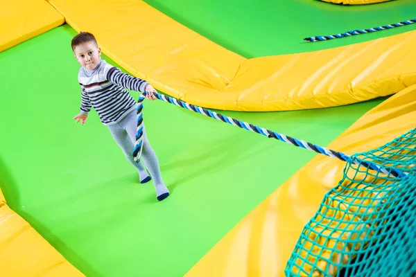 Niño jugando en el centro de trampolín saltando y subiendo con cuerda — Foto de Stock