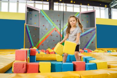 Oyun merkezindeki kuru havuzda yumuşak küplerle oynayan çocuklar. Trambolin kulübünde köpük blokları olan oyun alanı