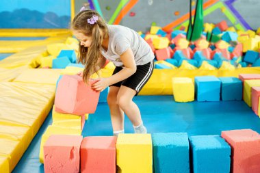 Oyun merkezindeki kuru havuzda yumuşak küplerle oynayan çocuklar. Trambolin kulübünde köpük blokları olan oyun alanı