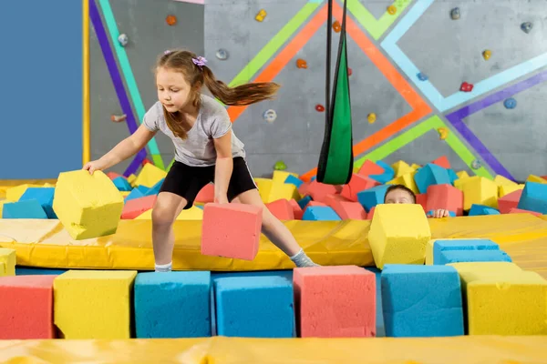Oyun merkezindeki kuru havuzda yumuşak küplerle oynayan çocuklar. Trambolin kulübünde köpük blokları olan oyun alanı