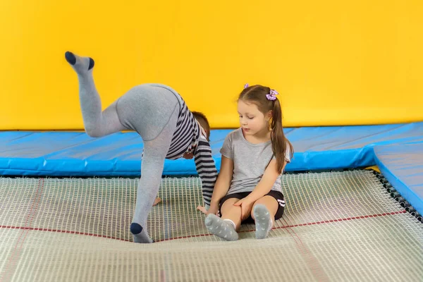 Feliz sonrisa niños pequeños sentados en el trampolín interior y jugando en el centro de entretenimiento —  Fotos de Stock