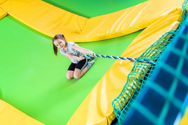 Girl playing in trampoline center jumping and climbing with rope — Stock Photo, Image