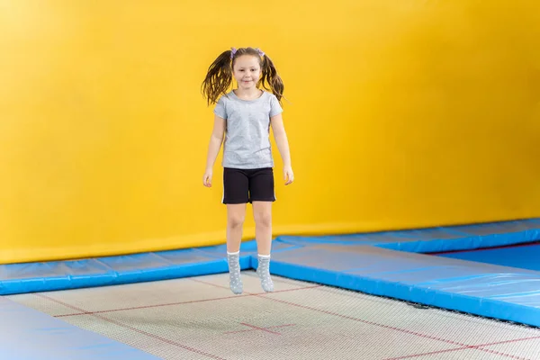 Happy little girl jumping on trampoline in fitness center — Stock Photo, Image
