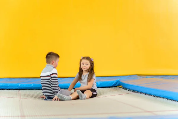 Feliz sonrisa niños pequeños sentados en el trampolín interior y jugando en el centro de entretenimiento —  Fotos de Stock