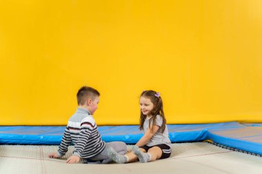 Mutlu gülümseyen küçük çocuklar trambolinde oturuyor ve eğlence merkezinde oynuyorlar.