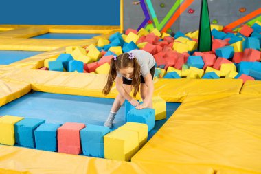 Oyun merkezindeki kuru havuzda yumuşak küplerle oynayan çocuklar. Trambolin kulübünde köpük blokları olan oyun alanı