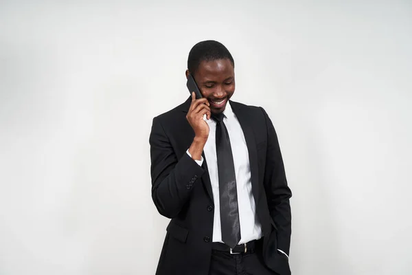 Retrato do homem africano sorrindo enquanto fala no telefone com parede cinza no fundo com espaço de cópia — Fotografia de Stock