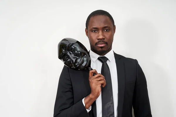 Jovem africano vestindo terno preto tirando máscara de plástico revelando rosto — Fotografia de Stock