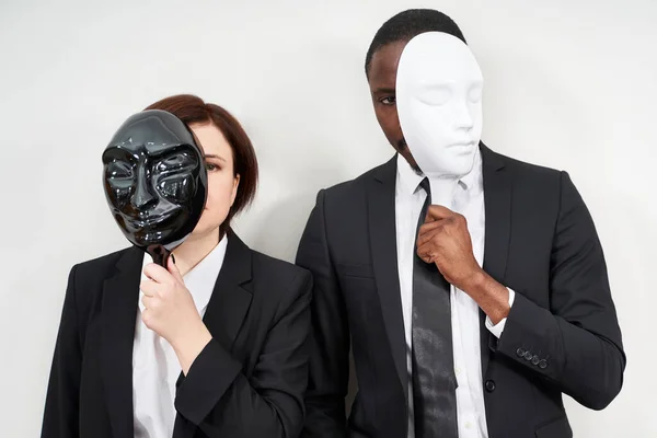 Homme africain et femme caucasienne portant des costumes noirs cachant visage avec des masques en plastique — Photo