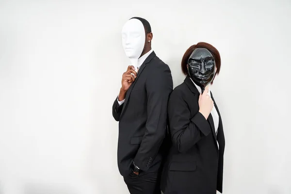 Homme africain et femme caucasienne portant des costumes noirs cachant visage avec des masques en plastique — Photo