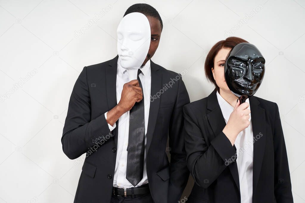 African man and Caucasian woman wearing black suits hiding face with plastic masks