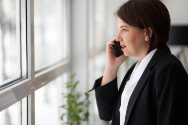 İş kadını ofis penceresinin yanında telefonla konuşuyor. Müdür, işveren..