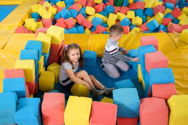 Oyun merkezindeki kuru havuzda yumuşak küplerle oynayan çocuklar. Trambolin kulübünde köpük blokları olan oyun alanı