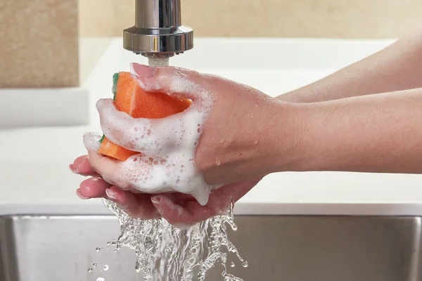 Обрезанное изображение женщины, держащей моющую губку с жидкостью для мытья посуды над раковиной, концепция очистки — стоковое фото