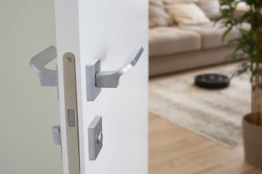Robotik elektrikli süpürge, rahat modern oturma odasında, açık kapılar ardında.
