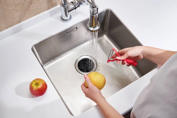 Großaufnahme einer Frau, die über der Spüle in der Küche Apfel schält — Stockfoto