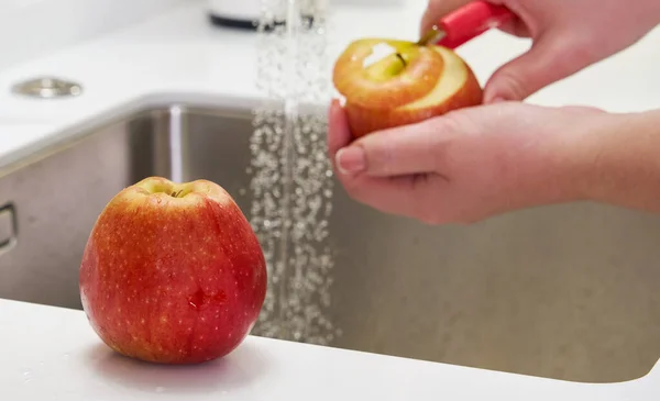 Primer plano de la mujer pelando manzana por encima del lavabo en la cocina — Foto de Stock