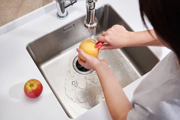 Primer plano de la mujer pelando manzana por encima del lavabo en la cocina — Foto de Stock