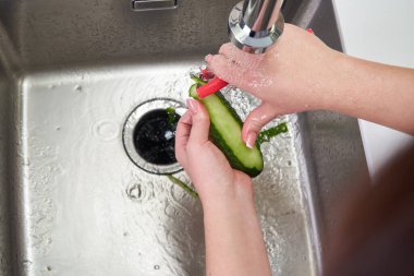 Modern mutfaktaki lavaboda salatalık soyan kadın ellerinin yiyecek öğütücü makinesinin üzerine kesilmiş görüntüsü.