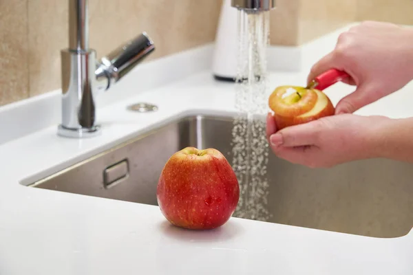 Primer plano de la mujer pelando manzana por encima del lavabo en la cocina — Foto de Stock