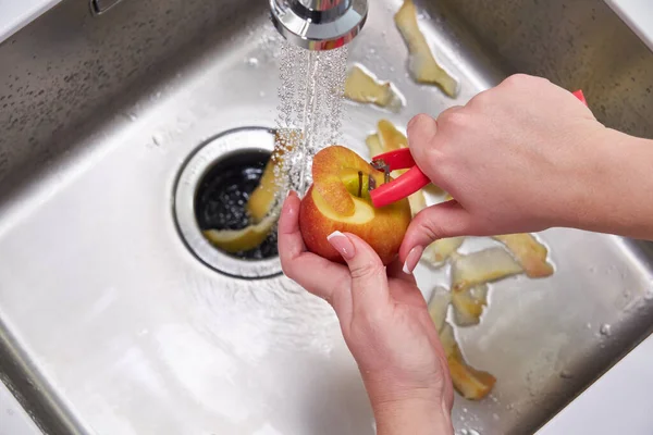 Καλλιεργημένη άποψη των γυναικείων χεριών ξεφλούδισμα μήλου πάνω από τη μηχανή διάθεσης απορριμμάτων τροφίμων — Φωτογραφία Αρχείου