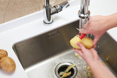 Modern mutfaktaki lavaboda patates soyarken kadın eli görüntüsü.