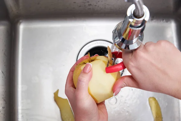 Обрезанный вид женских рук, очищающих яблоко над машиной по утилизации пищевых отходов — стоковое фото