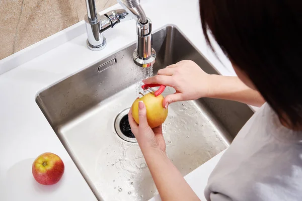 Primer plano de la mujer pelando manzana por encima del lavabo en la cocina — Foto de Stock