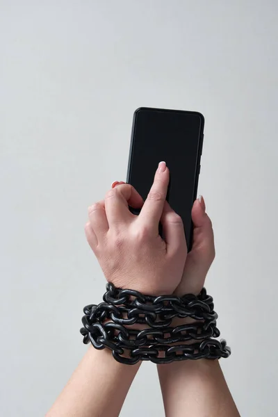 Iron chain that ties together hand and smartphone in concept of social media and internet addiction on gray background — Stock Photo, Image