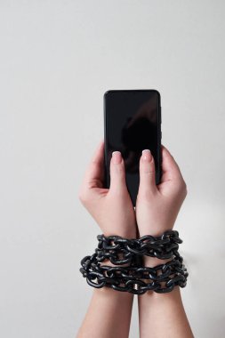 El ve akıllı telefonu sosyal medya ve internet bağımlılığı kavramına bağlayan demir zincir gri arka planda
