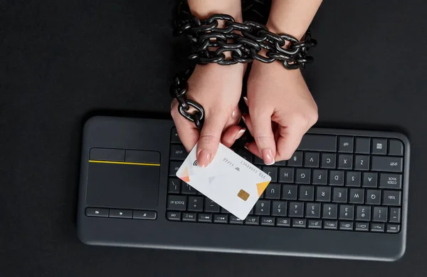 Mujer con cadena metálica sosteniendo tarjeta de crédito sobre el teclado, concepto de adicción a las compras en línea — Foto de Stock