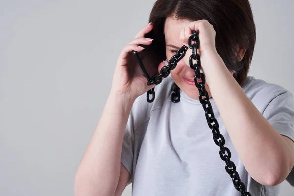 Femme parlant sur un téléphone portable enchaîné sur fond gris, concept de dépendance — Photo