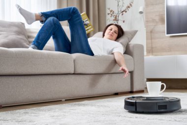 Robotik elektrikli süpürge bir kadına koltukta dinlenirken bir fincan kahve getiriyor.
