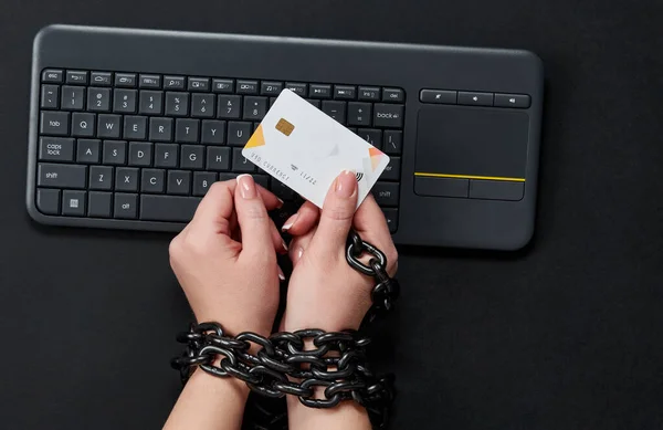 Mujer con cadena metálica sosteniendo tarjeta de crédito sobre el teclado, concepto de adicción a las compras en línea — Foto de Stock
