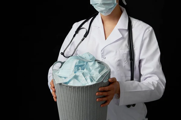 Läkaren håller hinken full av använda ansiktsmasker, kasta bort dem som symbol för epidemiska slut — Stockfoto