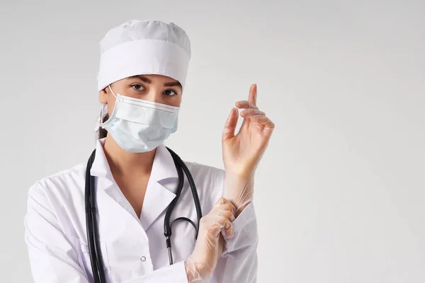 Молодой доктор надевает хирургические перчатки на белом фоне — стоковое фото