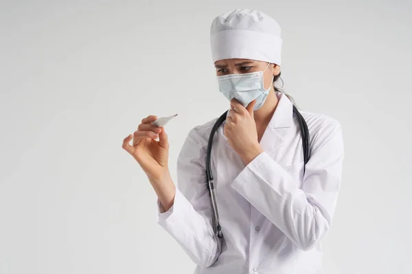 Läkare bär ansiktsmask tittar på mätning på medicinsk termometer över vit bakgrund med kopieringsutrymme — Stockfoto