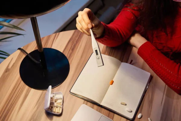 Kranke Frau mit Tabletten und Thermometer auf einem Tisch, die von zu Hause aus an einem Laptop auf Quarantäne-Isolation arbeitet. — Stockfoto