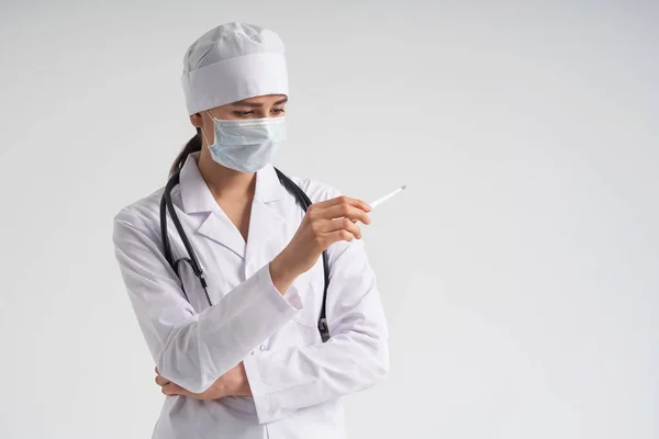 Läkare bär ansiktsmask tittar på mätning på medicinsk termometer över vit bakgrund — Stockfoto