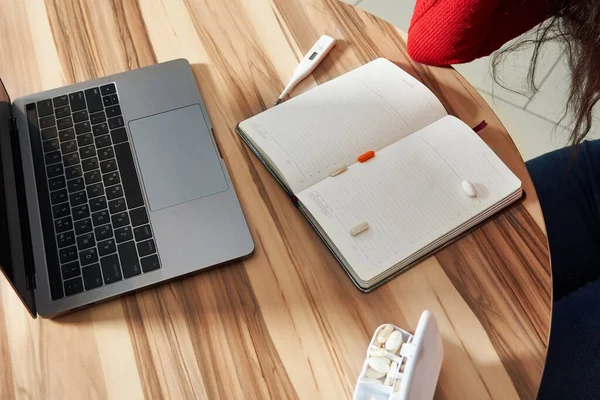 Kranke Frau mit Tabletten und Thermometer auf einem Tisch, die von zu Hause aus an einem Laptop auf Quarantäne-Isolation arbeitet. — Stockfoto