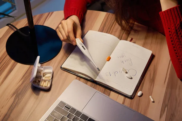 Kranke Frau mit Tabletten und Thermometer auf einem Tisch, die von zu Hause aus an einem Laptop auf Quarantäne-Isolation arbeitet. — Stockfoto